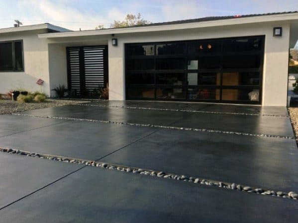 Concrete driveway with dark smooth slabs separated by pebble stone inlays for a modern design.