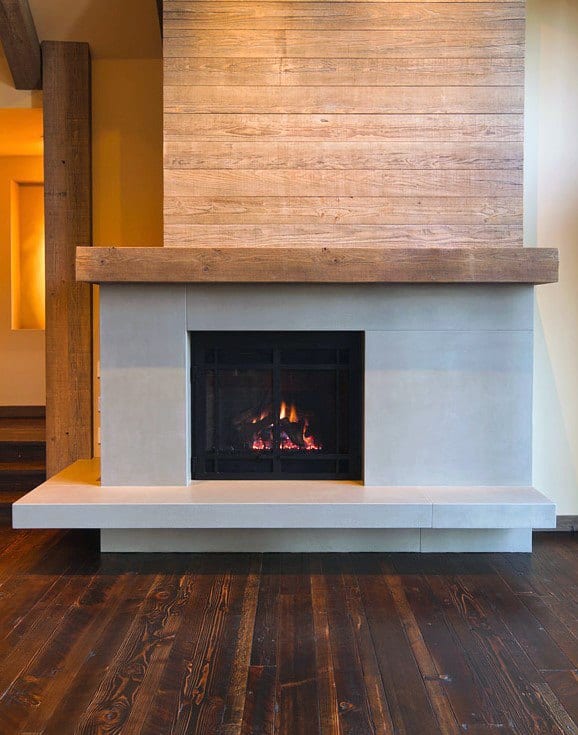 Rustic fireplace with concrete surround, wooden mantle, and warm wood-paneled backdrop.