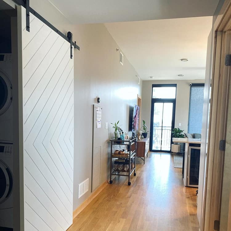 White sliding barn door in a modern condo hallway hiding a stacked washer and dryer unit.