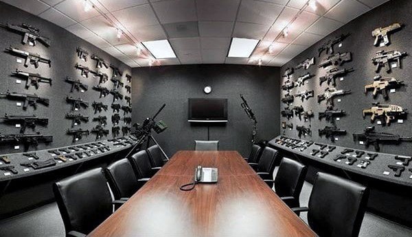 Conference room with firearms displayed on dark walls, central table, and chairs.