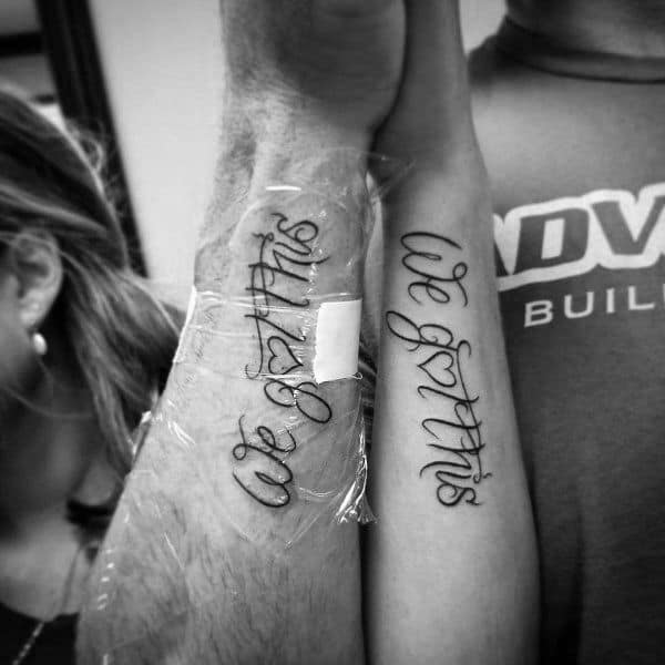 Matching forearm tattoos reading "we got this" in elegant script, symbolizing unity, support, and facing life’s challenges together.