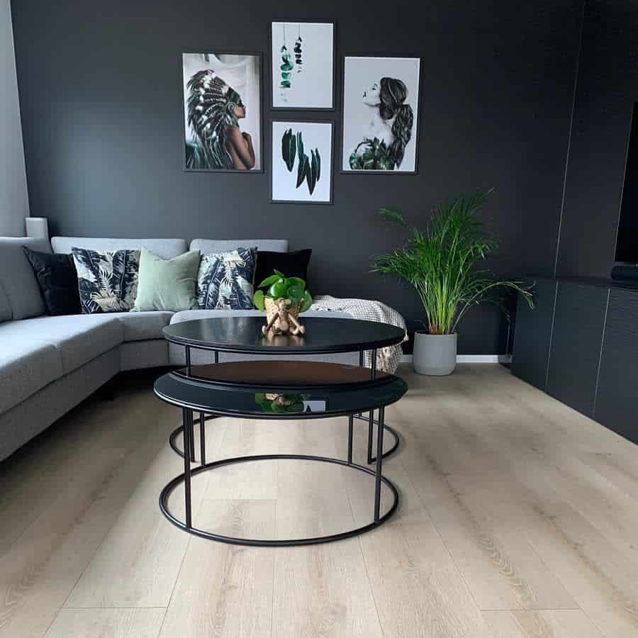 Modern living room with grey sectional sofa, black nested tables, wall art, and potted plant decor.