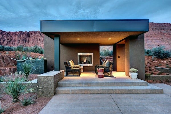 Modern flat-top pavilion with a fireplace, cozy seating, and desert landscape backdrop at dusk.