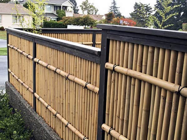 Metal-framed bamboo fence with horizontal bamboo supports in a suburban neighborhood setting.