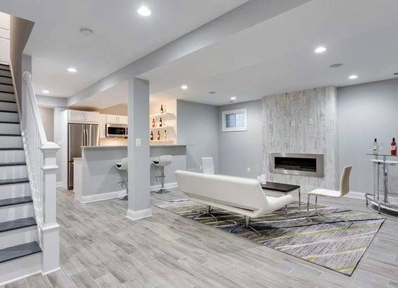 Contemporary basement with white and gray tones, open kitchen, living space, and modern fireplace.