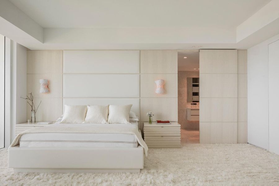 Minimalist bedroom with white platform bed, soft carpet, and neutral wall paneling.