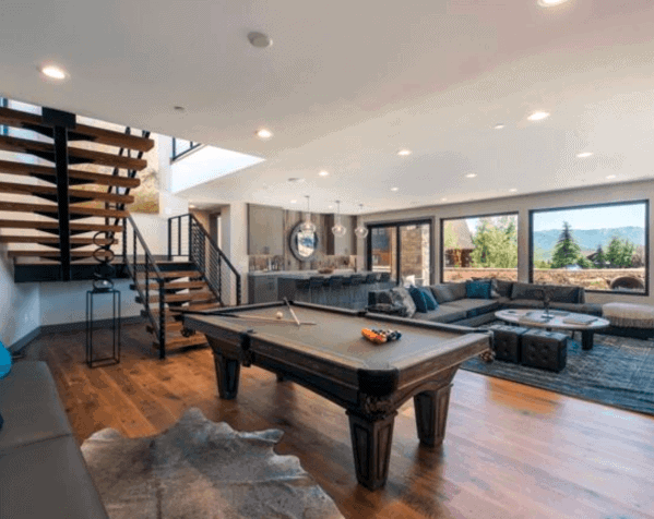 Contemporary billiard room with open layout, floating staircase, and large windows showcasing views.