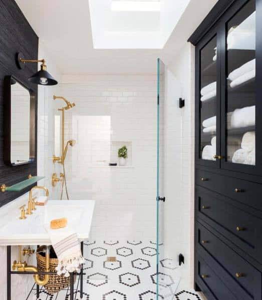 Black and white bathroom with gold fixtures, hexagon floor tiles, and glass shower.