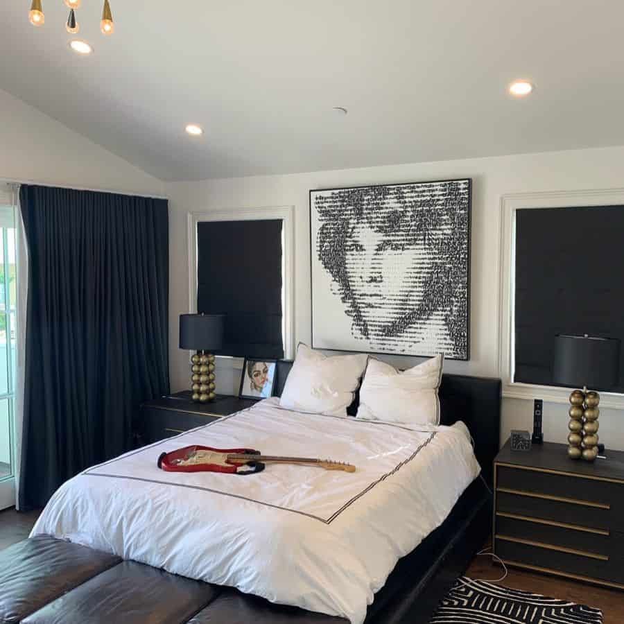 Modern bedroom with white bedding, black furniture, large portrait art, and two black lamps.