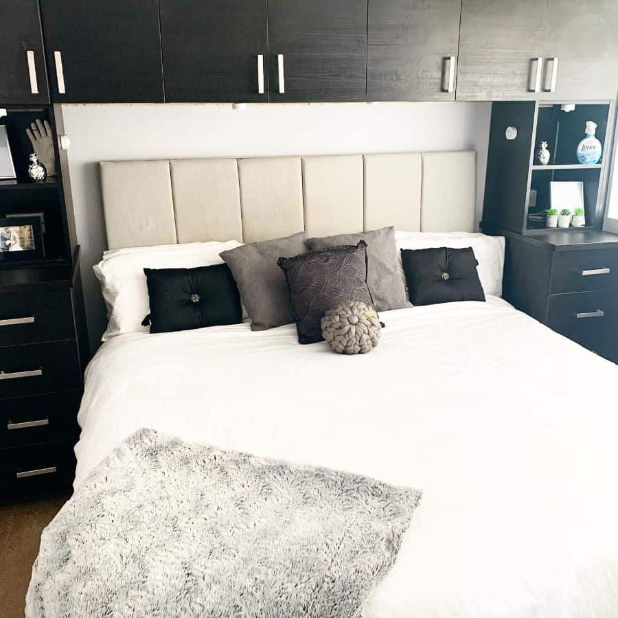 Modern bedroom with white bedding, grey upholstered headboard, and black cabinetry.