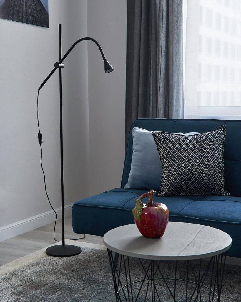 Minimalist living room with blue sofa, patterned pillow, black floor lamp, and round table.