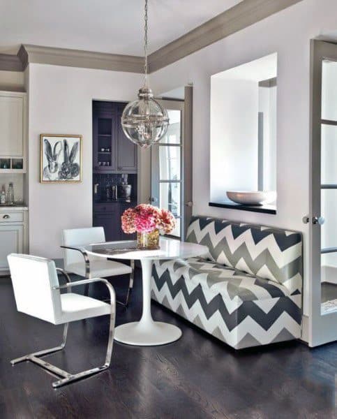Modern dining nook with chevron bench, tulip table, white chairs, pendant light, and pink flowers as centerpiece