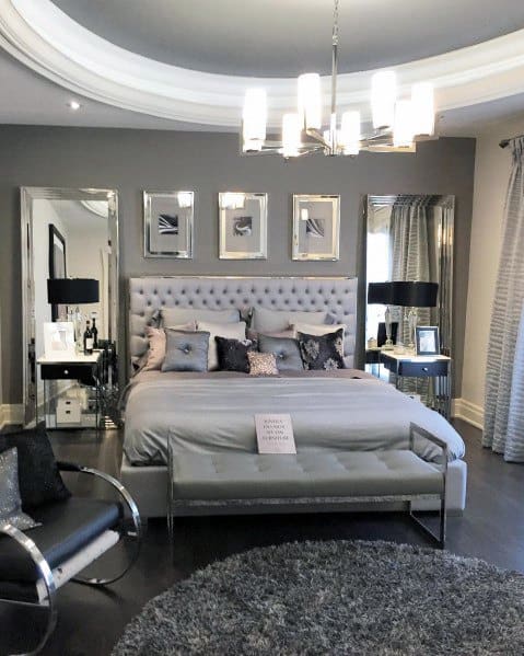 Luxury bedroom with tufted headboard, modern chandelier, mirrored decor, and gray accents.