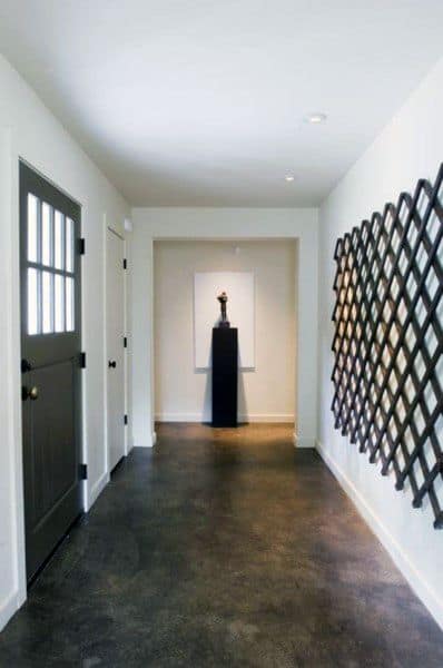 Minimalist hallway with a concrete floor, black door, grid wall pattern, and a sculpture on a pedestal at the end