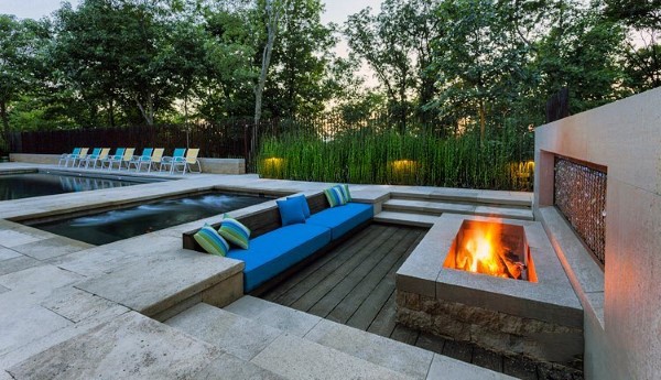 Contemporary patio with sunken seating, pool, fire pit, and lush greenery in the background.