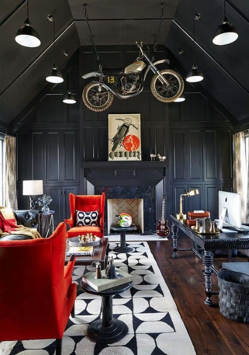 Man cave with dark walls, red chairs, a motorcycle hanging from the ceiling, and a patterned rug