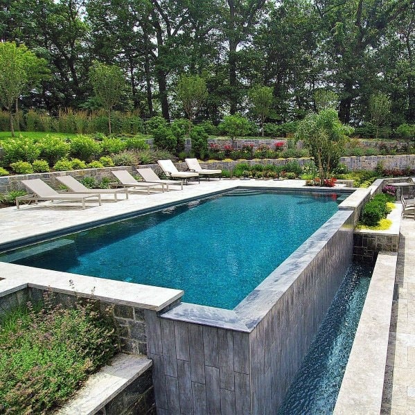 A luxurious rectangular pool with lounge chairs surrounded by lush greenery and landscaping