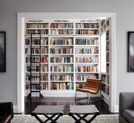 Cozy nook with a brown chair, ladder, and floor-to-ceiling bookshelf