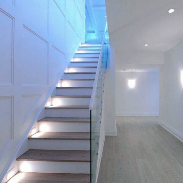 Modern staircase with glass railing and built-in LED step lighting in a bright white interior.
