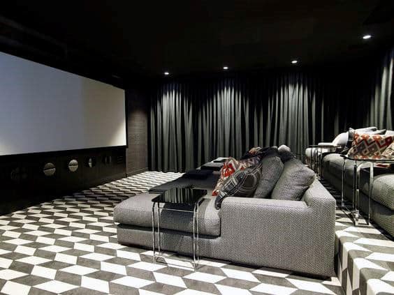 Modern home theater with gray seating, geometric flooring, and a large screen framed by black curtains