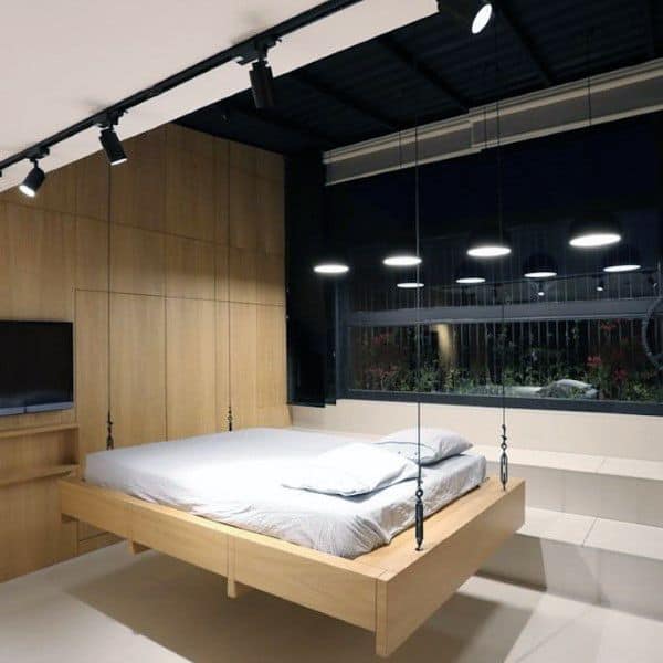 Minimalist hanging bed with sleek cables, wooden frame, and modern lighting in a contemporary room.