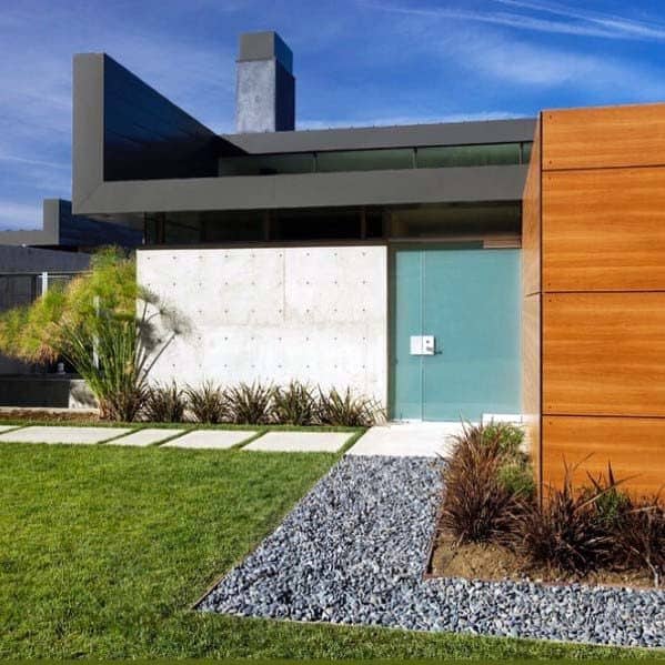 Modern home exterior with a sleek concrete wall, green door, and contemporary river rock landscaping along the pathway