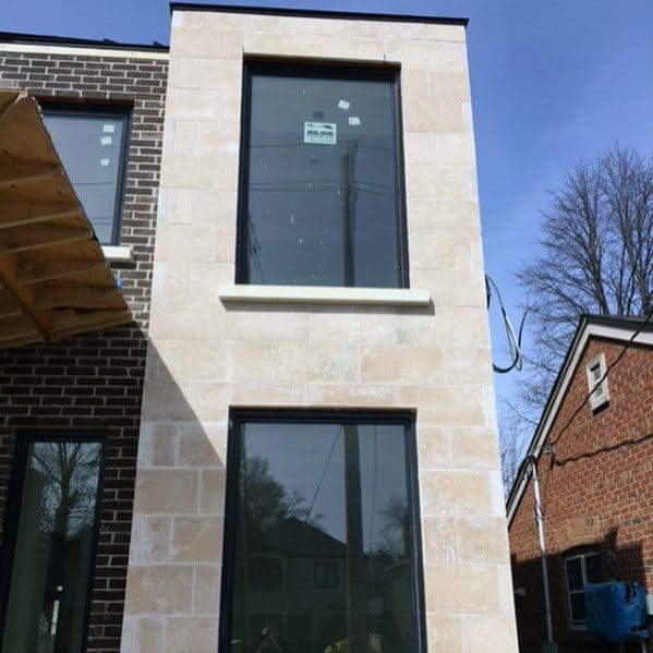 Contemporary home exterior with a mix of brick and limestone cladding, large black-framed windows, and modern architectural design