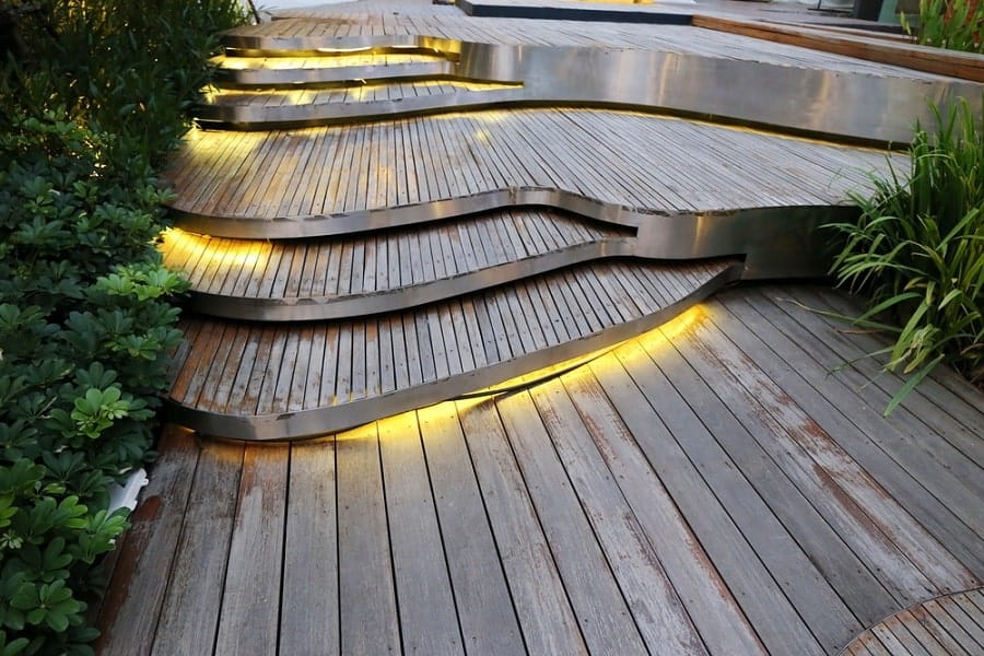 Curved wooden walkway with glowing lights, surrounded by greenery