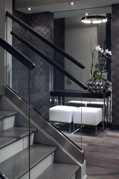 Modern interior featuring a chic staircase, black walls, sleek console table, white stools, and floral arrangement