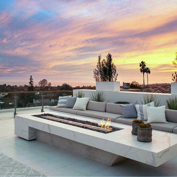 Modern rooftop patio with a marble fire pit, surrounded by a seating area, against a colorful sunset sky