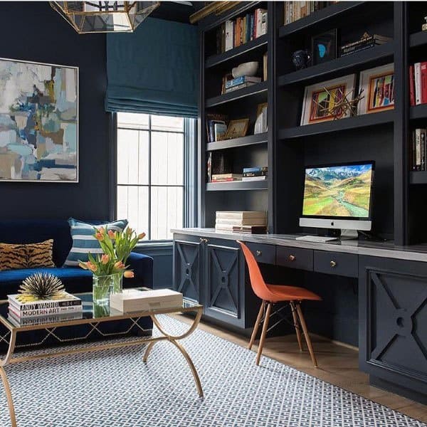 Contemporary home office with navy built-in shelves, orange chair, and modern decor accents.