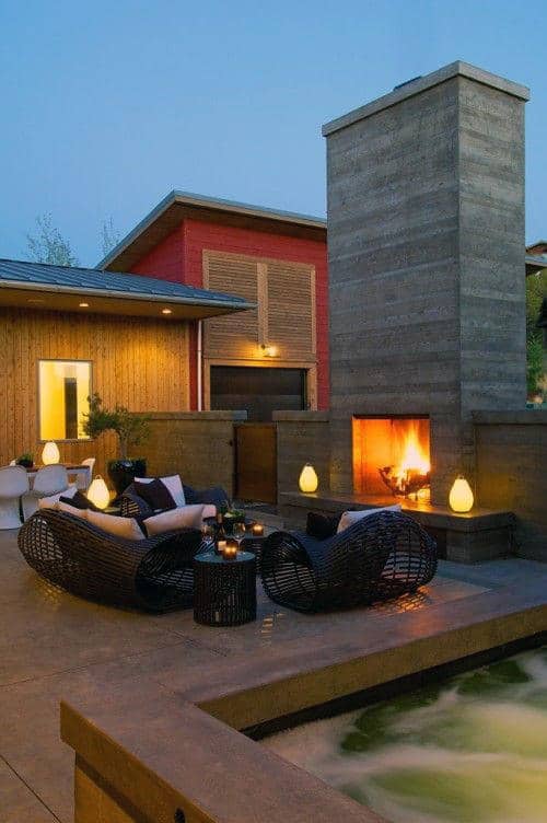 Cozy patio with wicker furniture, lit fireplace, and ambient lighting at dusk next to a small pool