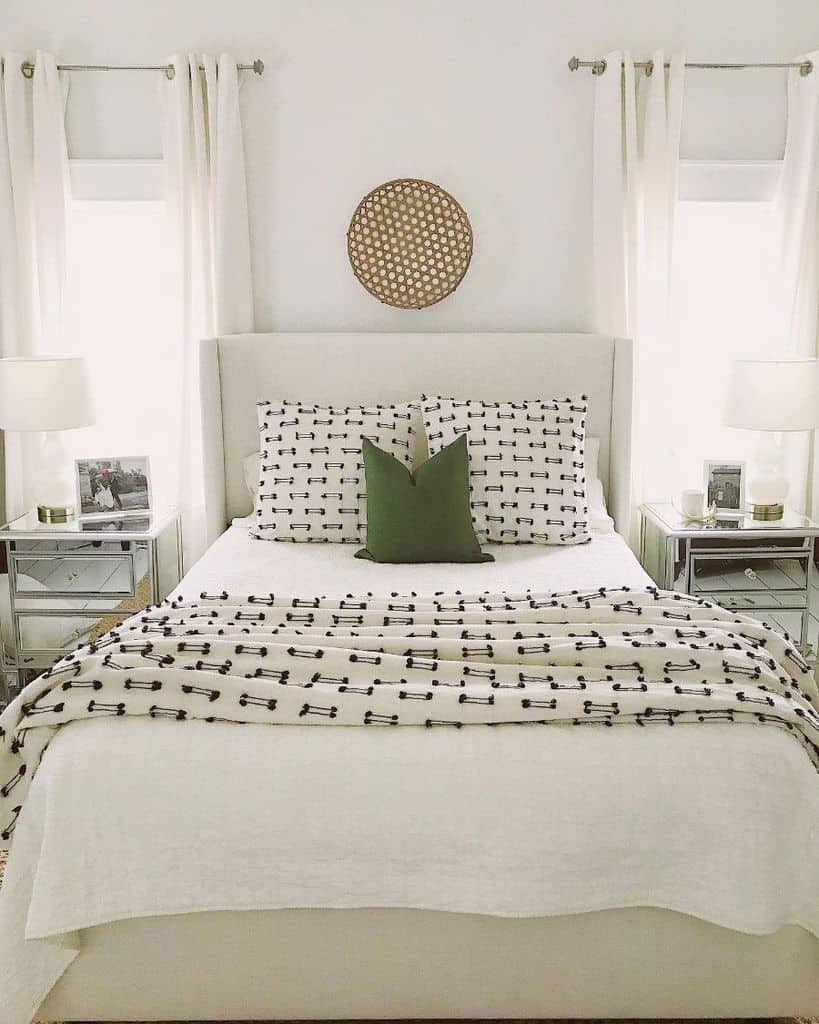 Cozy bedroom with a patterned bedspread, white bedside tables, green accent pillow, and lamps beside framed photos