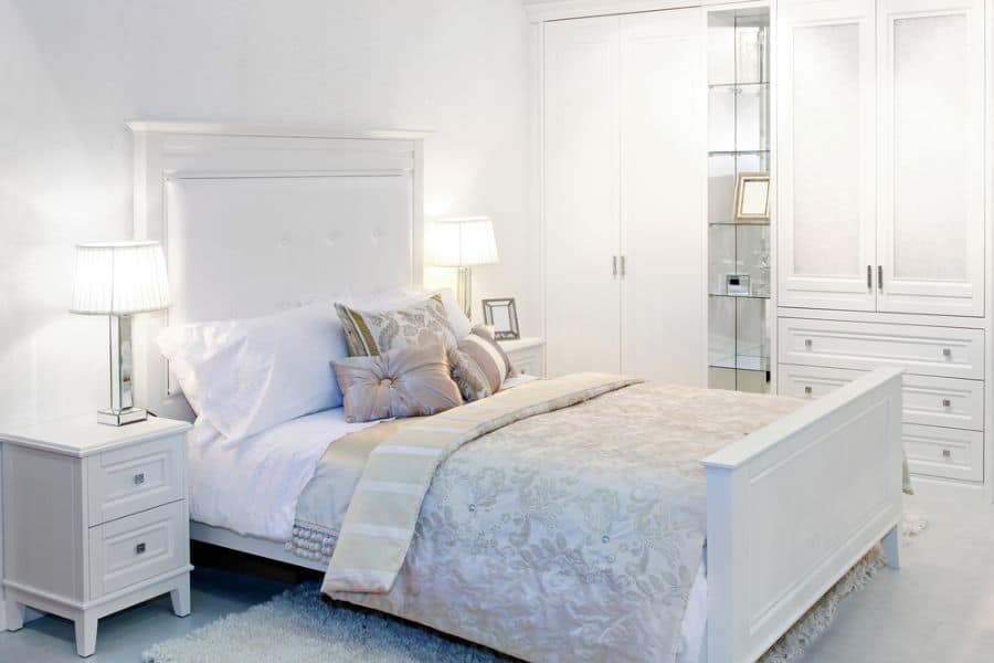 Bright white bedroom with a large bed, two nightstands featuring lamps, and a sleek wardrobe