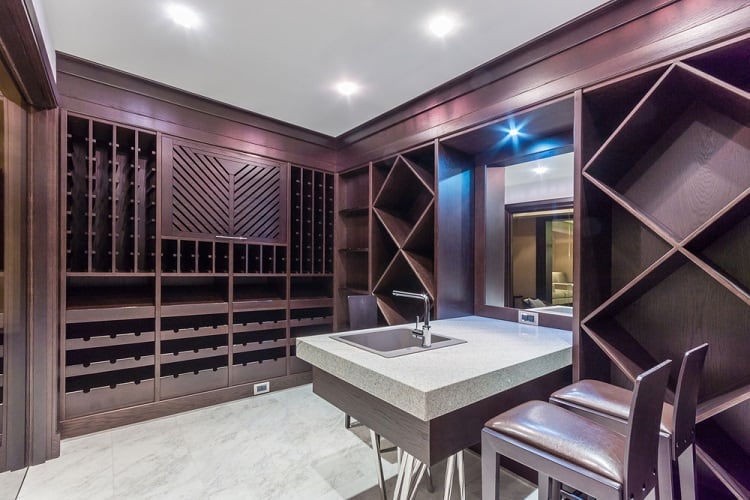 Modern wine cellar with dark wooden shelves, a sleek countertop, and built-in sink with seating.