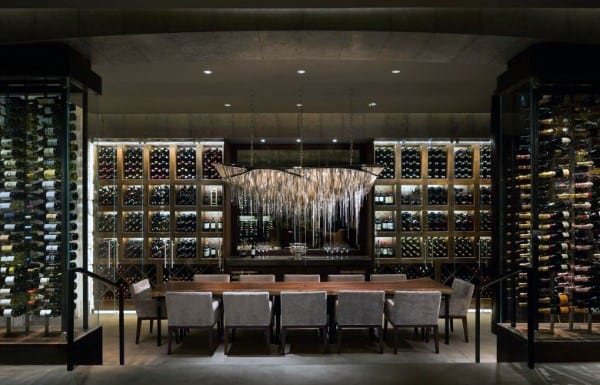 A luxurious wine cellar with shelves of fine wine bottles, a long table, and an elegant chandelier