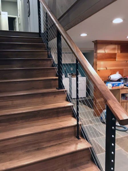 Wooden staircase with black cable railing in a basement featuring wood-paneled walls.