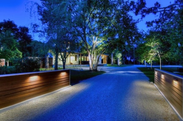 Contemporary driveway with wooden wall features and ambient lighting, illuminating the gravel path and surrounding trees