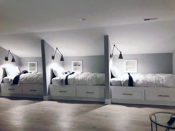 An attic bedroom with three built-in beds, each with overhead lamps and crisp white bedding