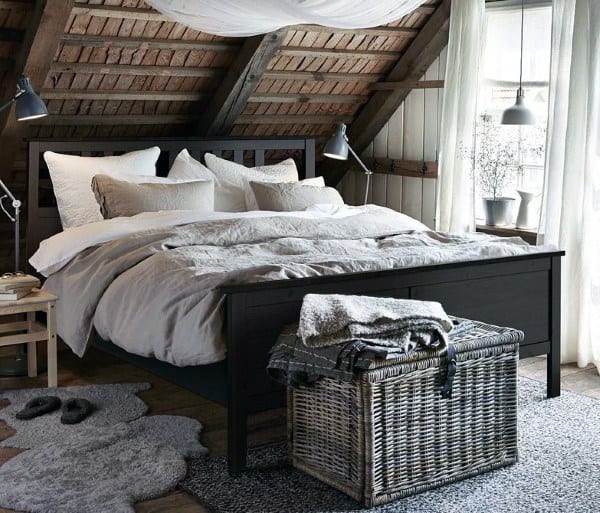 Cozy attic bedroom featuring a wooden bed, soft bedding, a wicker trunk, and large windows with sheer curtains