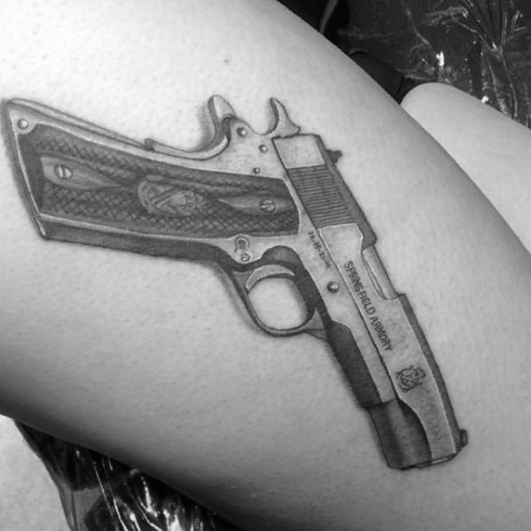 Realistic black and gray tattoo of a Springfield Armory 1911 pistol on the thigh, featuring fine details and shading for a lifelike effect.