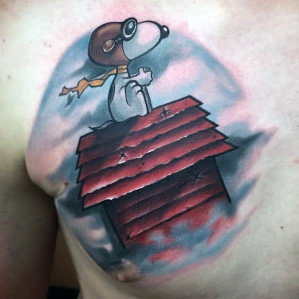 Colorful tattoo of Snoopy as a flying ace, wearing goggles and a scarf, sitting on his red doghouse, surrounded by clouds on a chest.