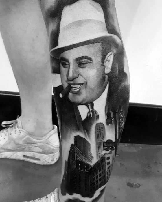 Al Capone tattoo featuring a detailed black-and-white portrait of the gangster with a cigar, surrounded by city skyscrapers and a vintage scene.