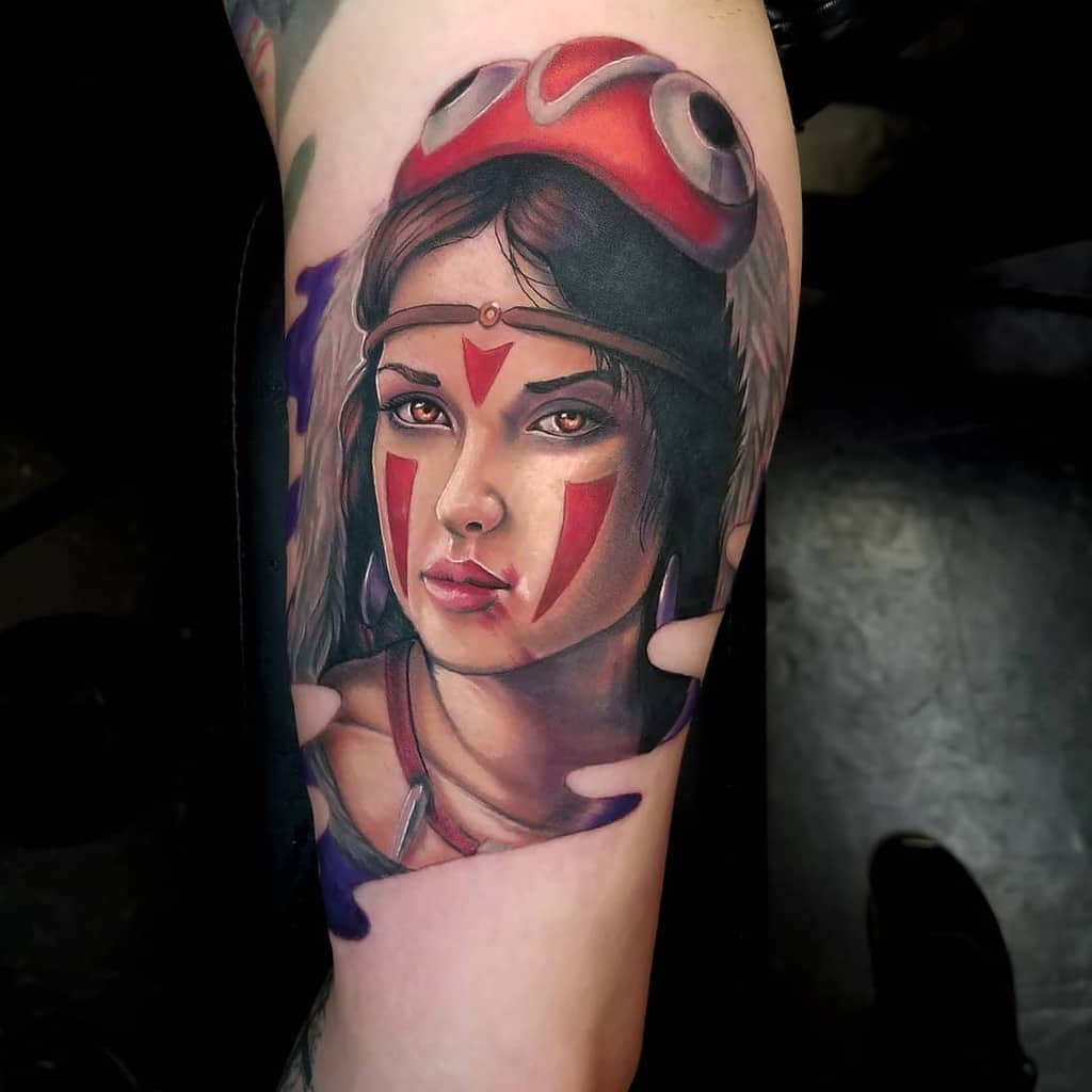 Vibrant and detailed tattoo of a young woman wearing a red tribal mask and face markings. The artwork features a lifelike depiction of her face, with piercing eyes and subtle shading to create depth and realism, showcasing her strong yet serene expression.