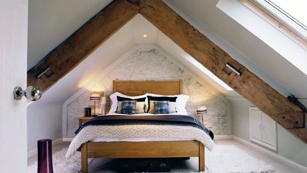 Cozy attic bedroom with wooden beams, a rustic wooden bed, white bedding, and a skylight