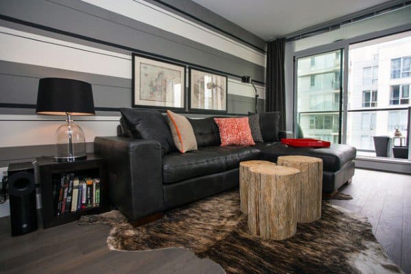 Modern living room with a dark leather sectional sofa, cowhide area rug, and wooden stump coffee tables.