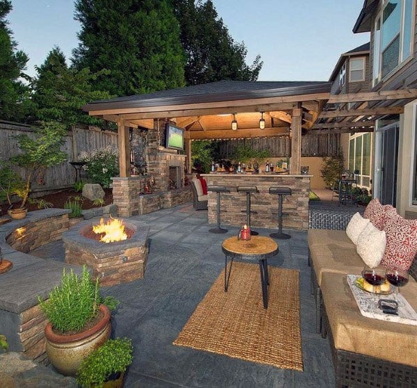 Cozy outdoor bar with a stone fire pit, wooden pavilion, barstools, and a sectional seating area.