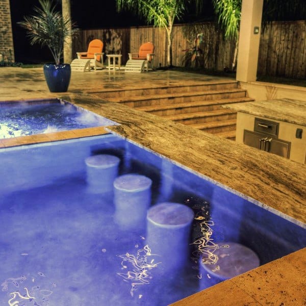 Poolside bar with underwater seating, stone countertop, and cozy outdoor lounge area.