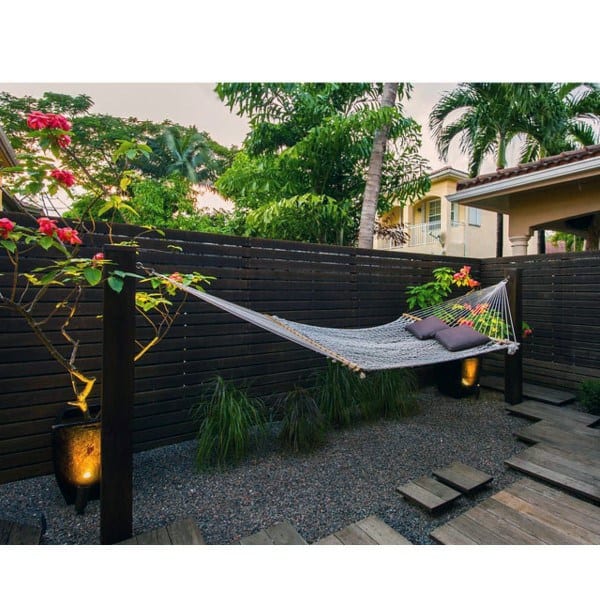 Relaxing backyard with a hammock, tropical plants, wooden privacy fence, and soft lighting.