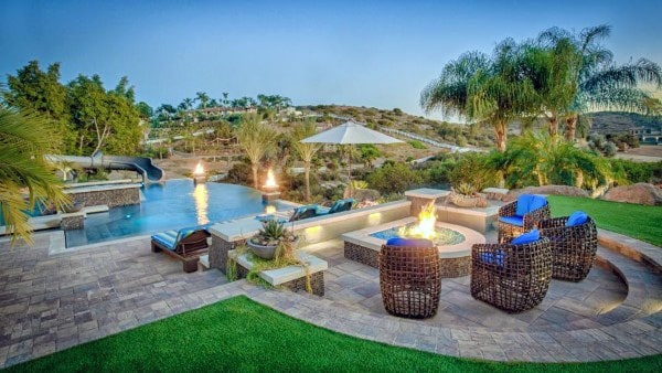 Backyard with infinity pool, water slide, fire pit, wicker chairs, and lush tropical landscaping.